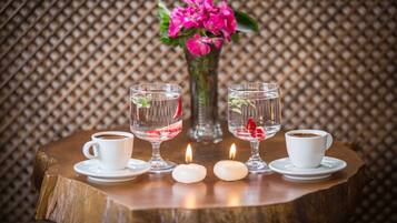 Una mesa con dos tazas de café blanco, dos vasos con agua y fresas, un jarrón con flores rosadas y dos velas encendidas.