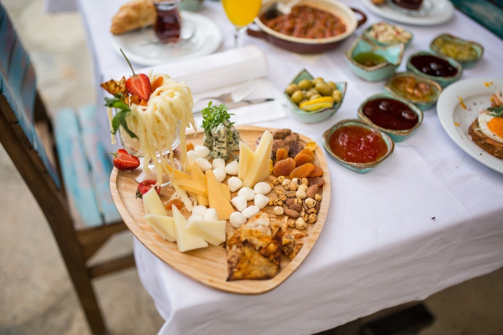 A table with a variety of cheeses, nuts, and fruits, along with small bowls of sauces and a croissant.