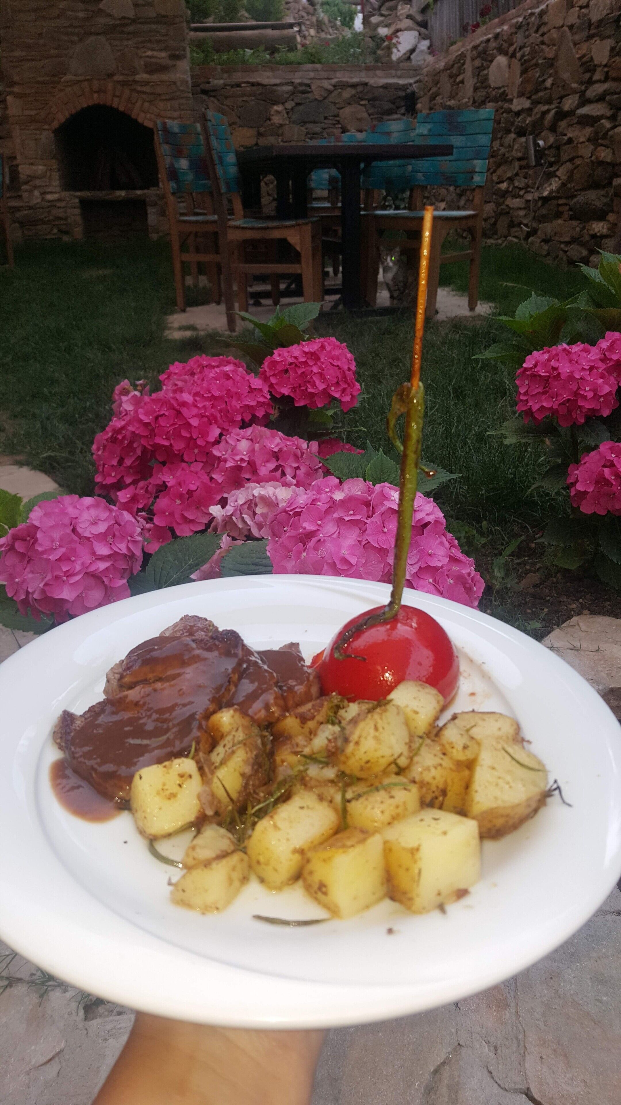 Un plato de comida con bistec, papas y una cereza sobre un plato blanco.