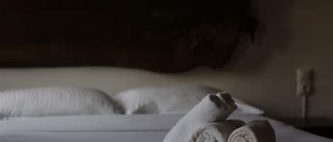 Una cama bien hecha con toallas enrolladas y una colcha estampada.