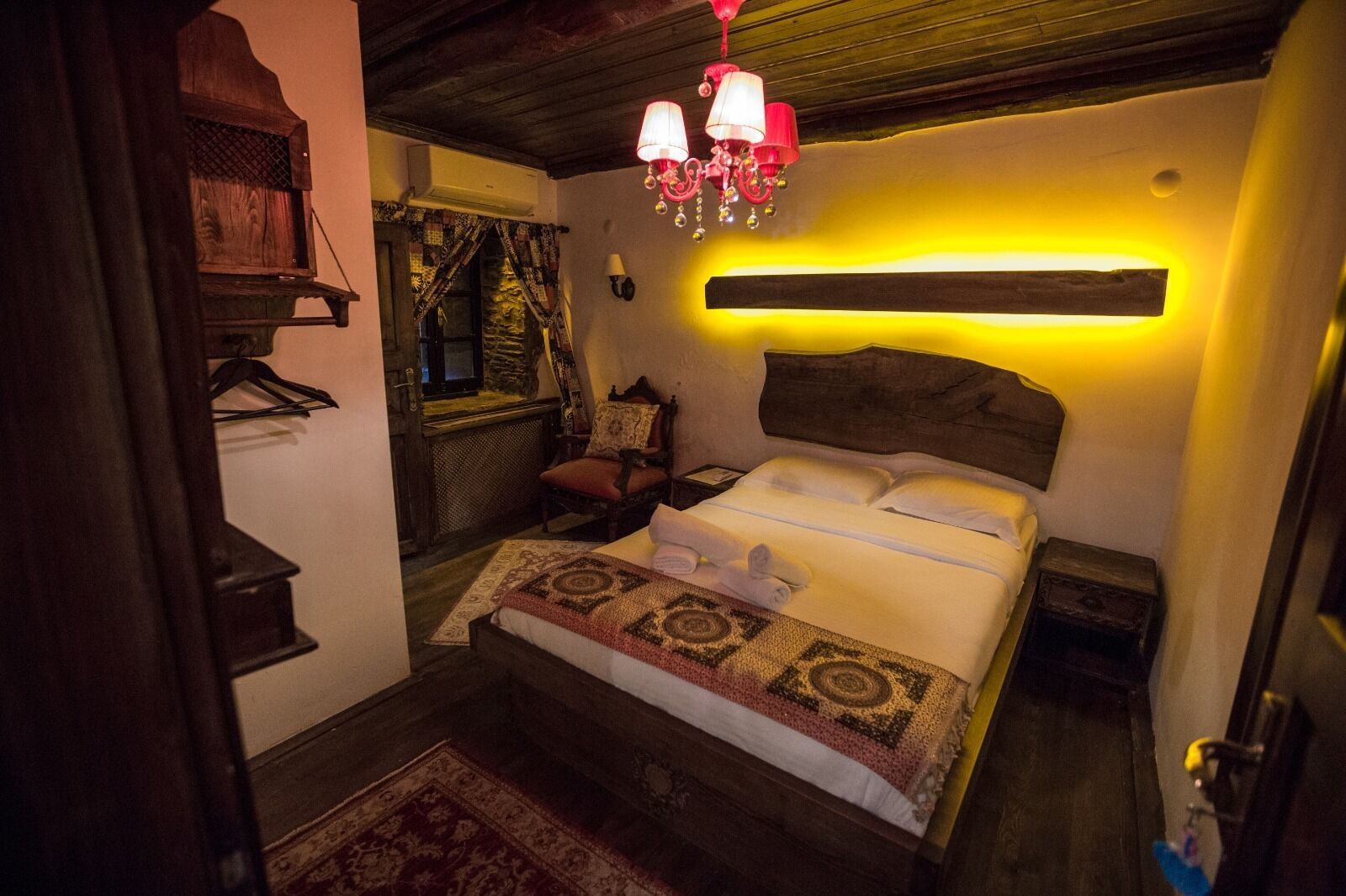 A cozy room with a bed, a wooden headboard, a hanging lamp, and a patterned rug.