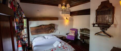 Un dormitorio con un cabecero de madera grande, una lámpara de araña colgante, un sillón morado y un perchero de madera.