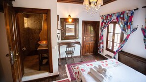 A room with a bed, a desk, a chair, a bathroom with a mosaic wall, and a chandelier. - Chez Rumi Butik Otel (Selçuk)