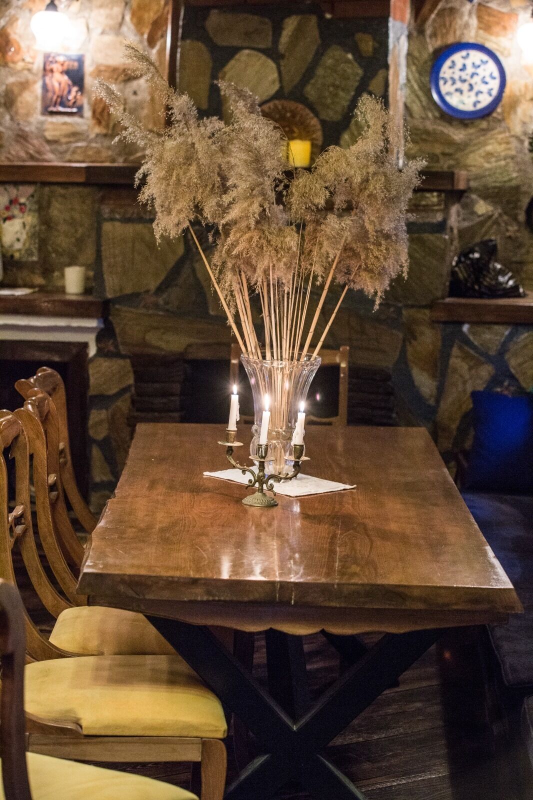A wooden dining table with a clear glass vase containing dried flowers and candles.