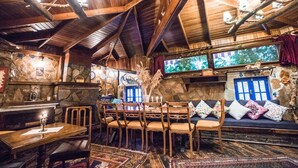 A rustic interior with wooden beams, stone walls, a stone fireplace, a dining area with wooden chairs, and a sofa with colorful cushions. - Chez Rumi Butik Otel (Selçuk)