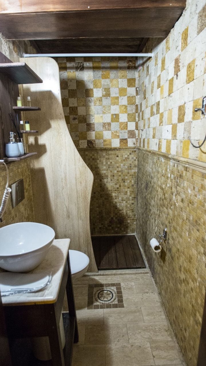 Un baño con pared de baldosas a cuadros, un tocador de madera con lavamanos y una zona de ducha.