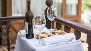 A table with a bottle of wine, two glasses, and a plate of food on a balcony. - Chez Rumi Butik Otel (Selçuk)