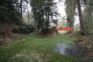Un puente rojo en una zona boscosa con un sendero cubierto de hierba y un pequeño arroyo.