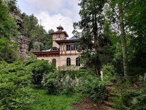 Ein historisches Gebäude mit einem Turm, umgeben von dichtem Wald und steilen Felsen.