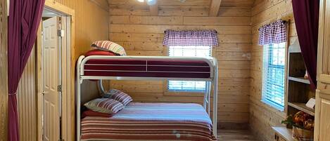 Una habitación de cabaña de madera con literas, ventilador de techo y ventana con persianas.