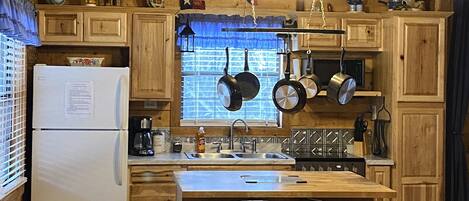 A cozy kitchen with wooden cabinets, a central island with bar stools, a refrigerator, and hanging pots.