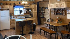Une cuisine chaleureuse avec des poutres en bois, un îlot central, des tabourets de bar, une table à manger et une horloge au mur.