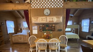 L’intérieur d’un chalet accueillant, avec une table et des chaises en bois, une horloge au mur et une fenêtre avec des rideaux.