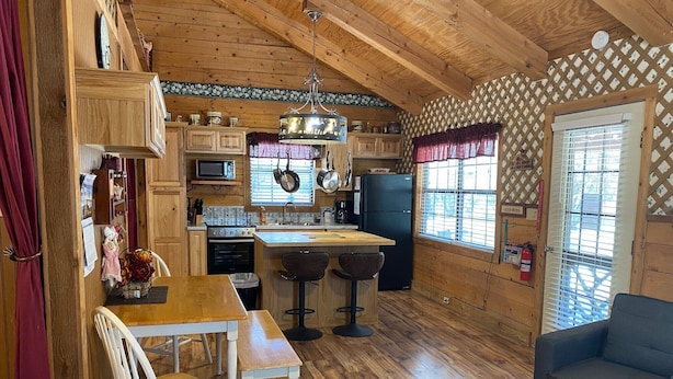 Une cuisine chaleureuse, aménagée dans le style d’un chalet, avec un plancher en bois, une table à manger avec des chaises, un coin bar et un canapé bleu.