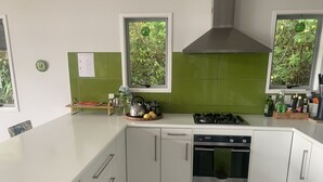 A modern kitchen with white cabinets, a gas stove, a dishwasher, and a window with a view of greenery. - Laze by the Lake - Holiday Home - Stunning Views of Lake Rotoiti  (Tikitere)