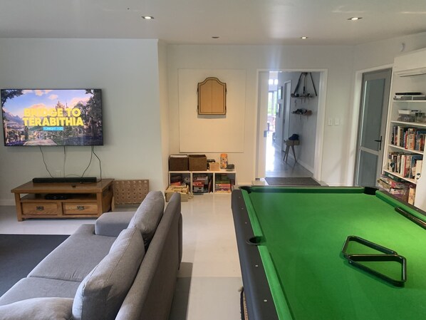 A living room with a pool table, a television, a sofa, and a bookshelf.
