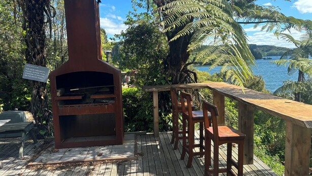 A wooden deck with a brick oven, seating, and a view of a lake. - Laze by the Lake - Holiday Home - Stunning Views of Lake Rotoiti  (Tikitere)