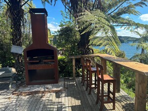 A wooden deck with a brick oven, seating, and a view of a lake.