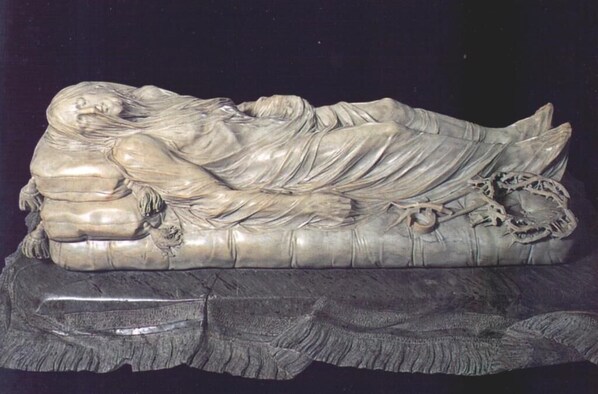 Une sculpture représentant une figure allongée, posée sur un socle sombre à la texture marquée.