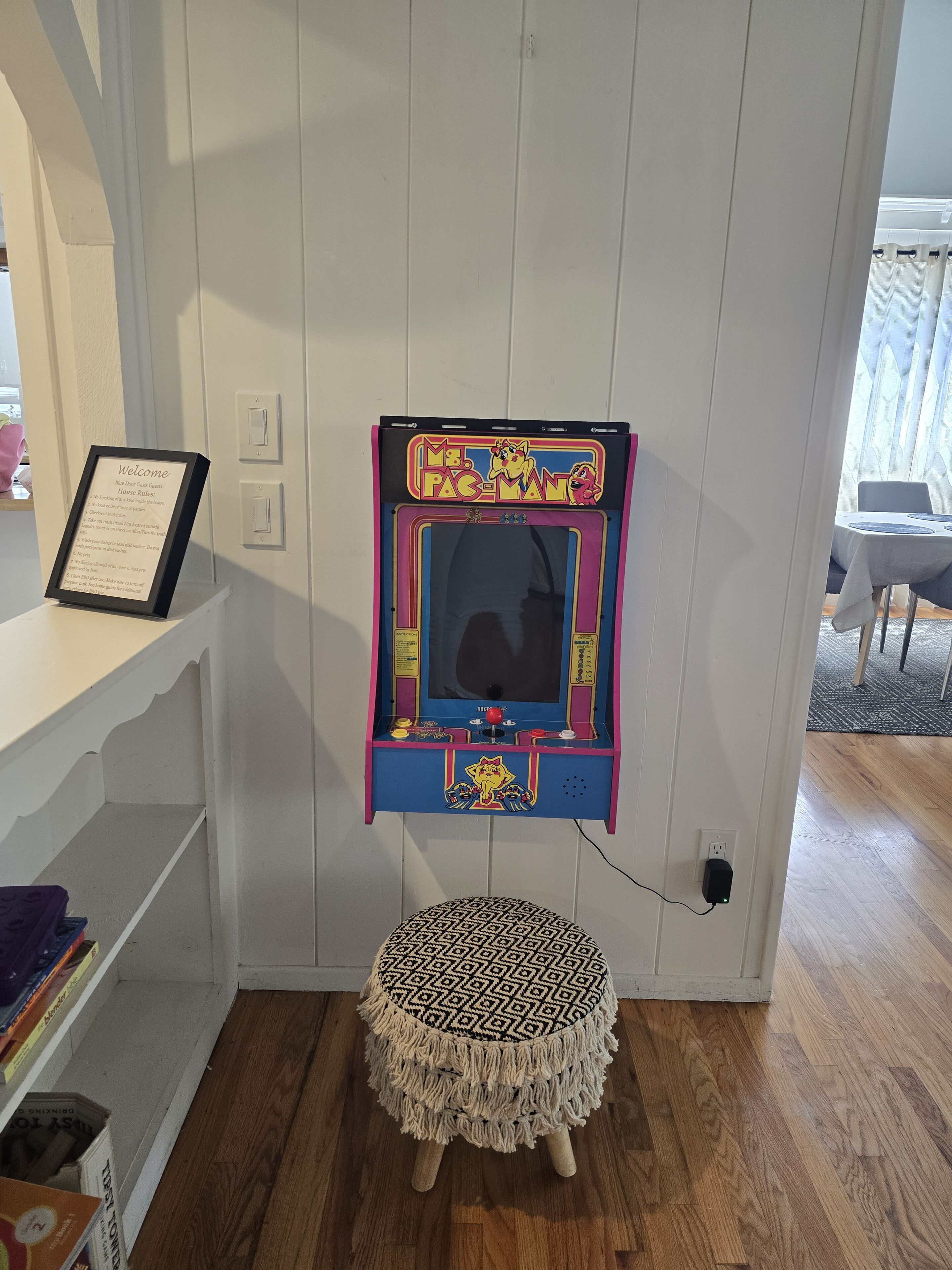 Een Pac-Man automaat bevestigd aan een muur, een lijst met een welkomstbord en een gestreept voetenbankje.