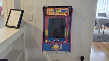 Een Pac-Man automaat bevestigd aan een muur, een lijst met een welkomstbord en een gestreept voetenbankje.