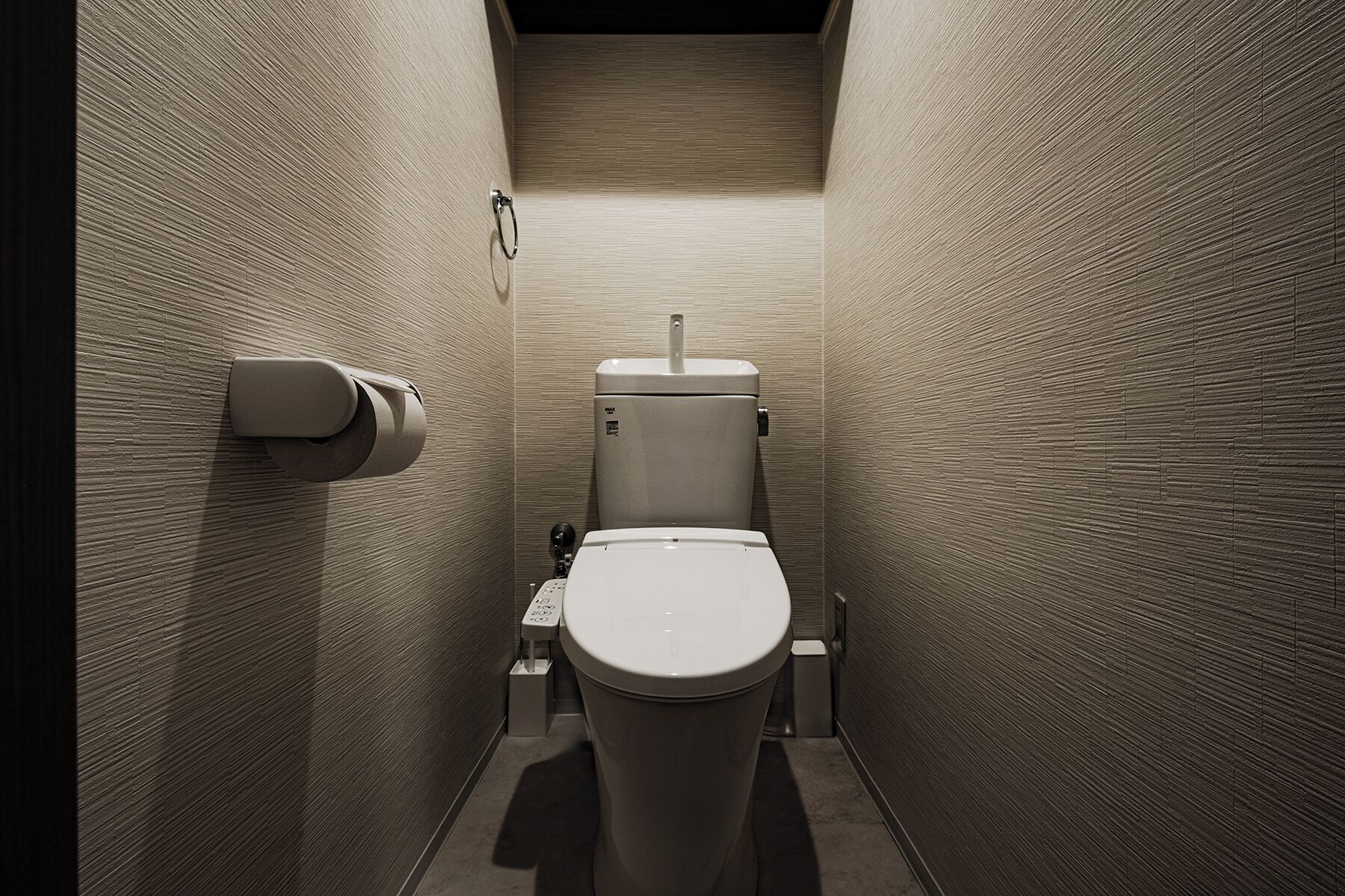 A narrow, modern bathroom with a toilet, a paper towel dispenser, and a hand dryer.