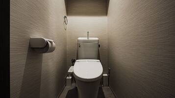 A narrow, modern bathroom with a toilet, a paper towel dispenser, and a hand dryer.