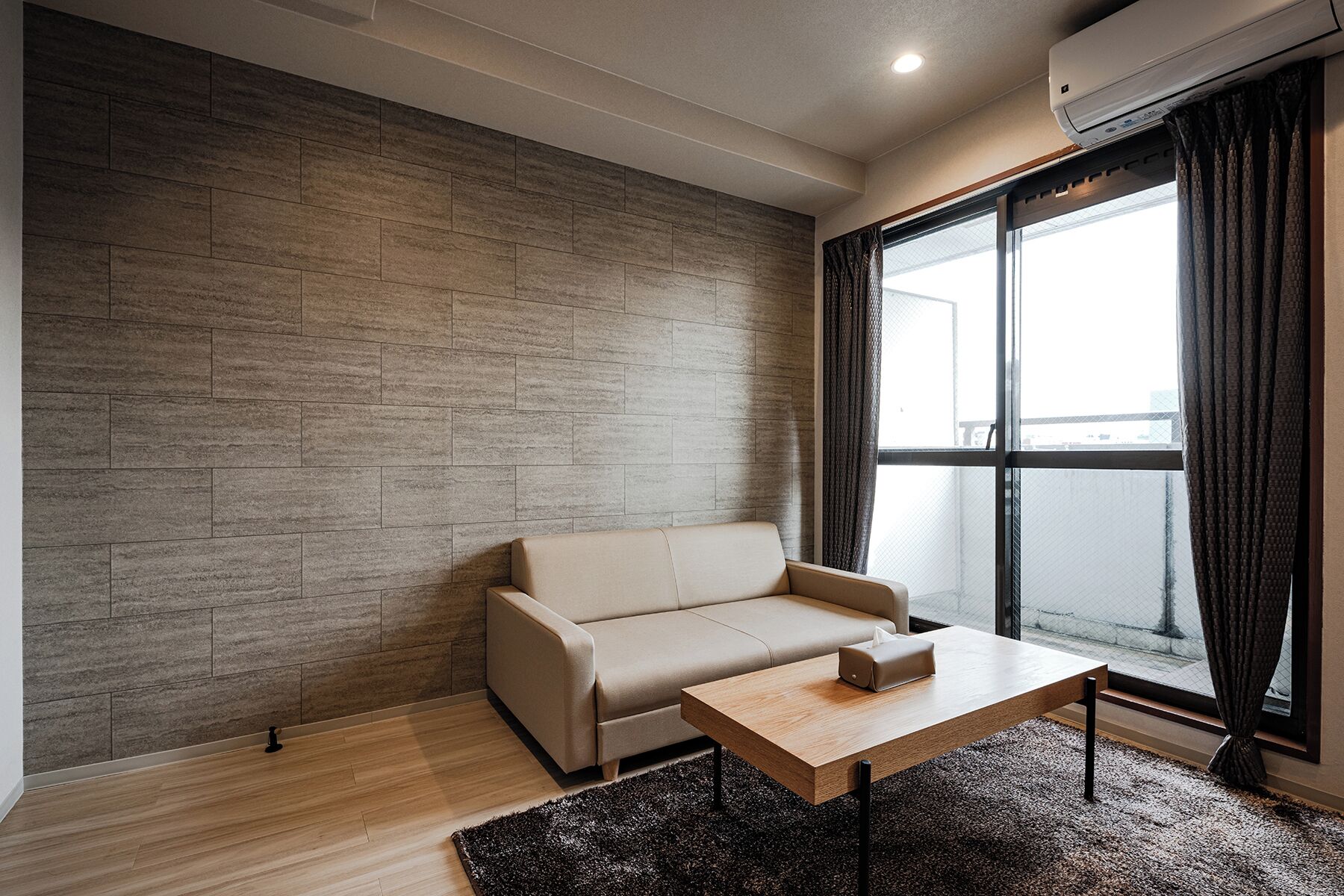 Un salon moderne avec un canapé beige, une table basse en bois et une grande fenêtre agrémentée de rideaux.