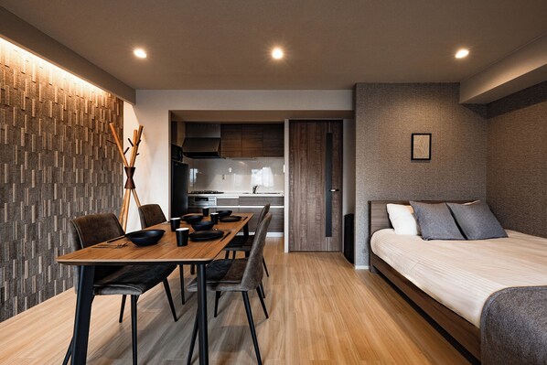 A modern bedroom with a bed, a dining area with a table and chairs, and a kitchen in the background. - Crice Hotel Namba II (Osaka)