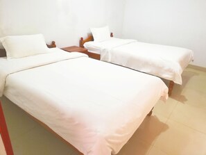 Two single beds with wooden headboards and white bedding, set in a clean and simple room with a tiled floor.