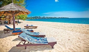 Relax on the beach with lounge chairs and a shaded thatched structure.