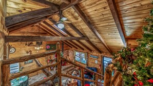 A rustic cabin interior with wooden beams, a staircase, and a Christmas tree.