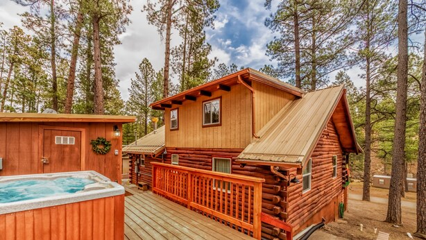 A log cabin with a hot tub, deck, and a view of the surrounding forest.