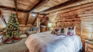 A cozy log cabin bedroom with a large bed, a Christmas tree, and a rustic wooden ceiling.
