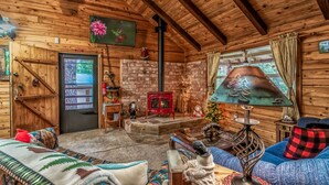 A cozy cabin interior with a fireplace, wooden walls, a sofa, and a Christmas tree.