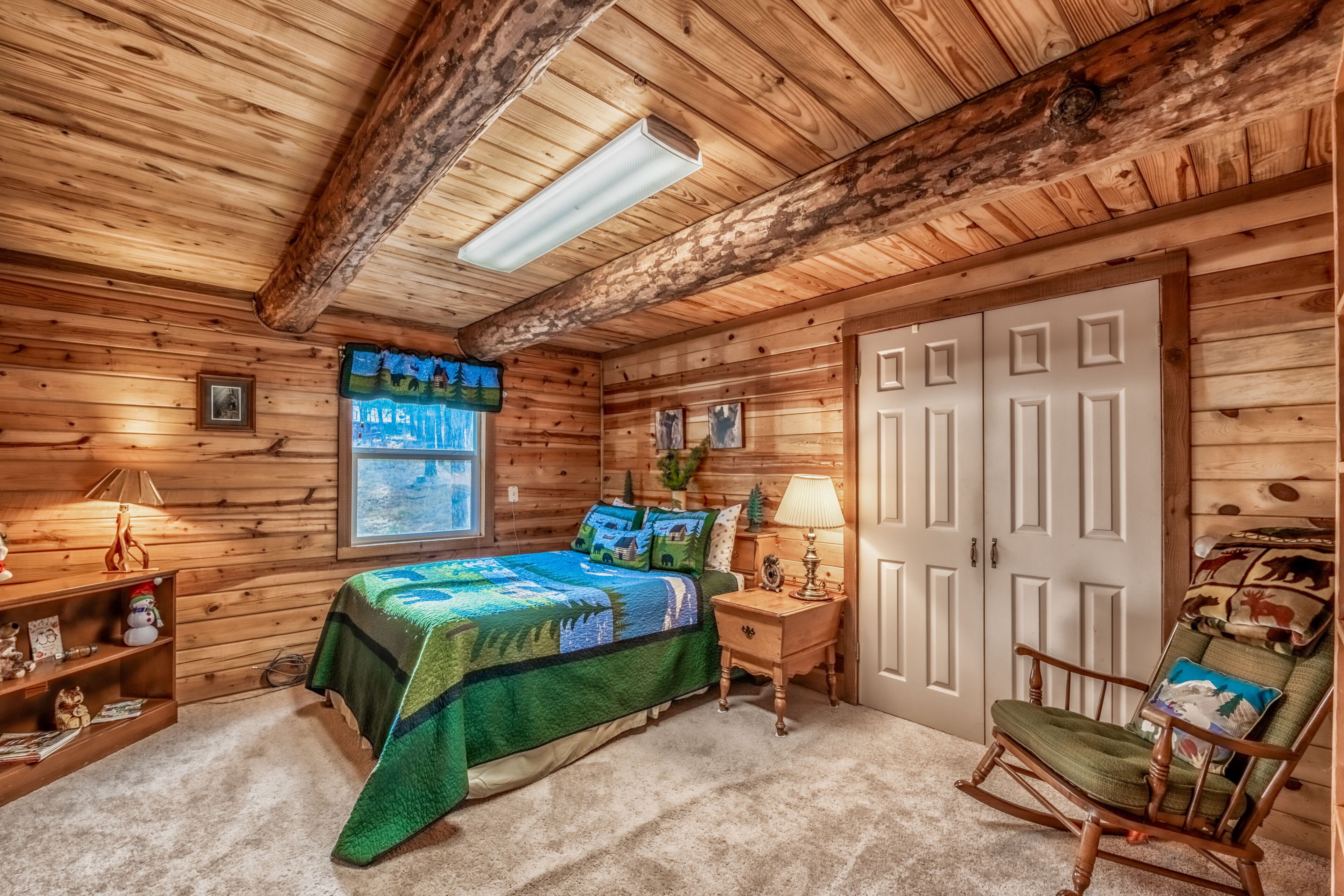 Ein gemütliches Schlafzimmer in einer Blockhütte mit Bett, Schaukelstuhl und Fenster mit Blick.
