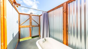 A compact, enclosed bathroom with a bathtub, shower, and wooden-framed window. - Waimea Beach Cottage by Destination Kauai - Charming 2BD, A/C, Walk to Ocean/Pier (Waimea)