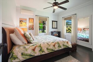 Une chambre à coucher avec un lit, un ventilateur de plafond, une fenêtre avec des rideaux et des œuvres d’art murales.