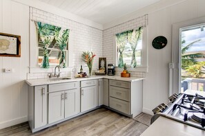 A modern kitchen with white cabinetry, a wooden countertop, and a gas stove. - Waimea Beach Cottage by Destination Kauai - Charming 2BD, A/C, Walk to Ocean/Pier (Waimea)