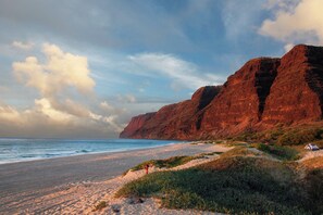 Une plage bordée de falaises rouges, un ciel dégagé et une tente plantée dans le sable.