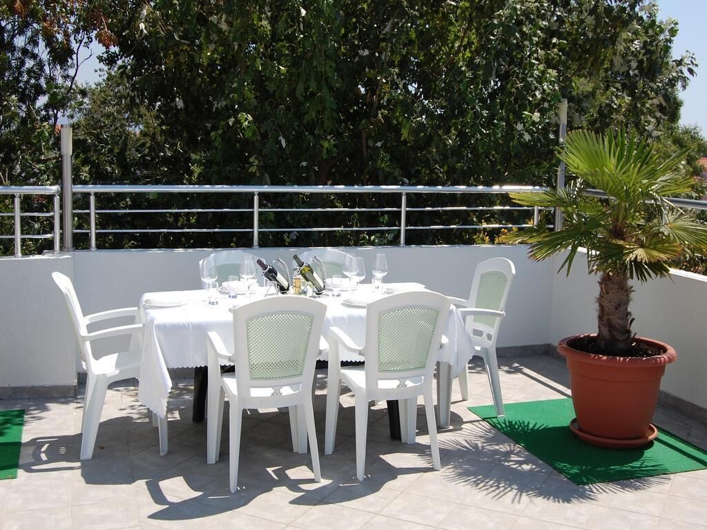 An outdoor dining area with a white table and chairs, a potted plant, and a green mat.