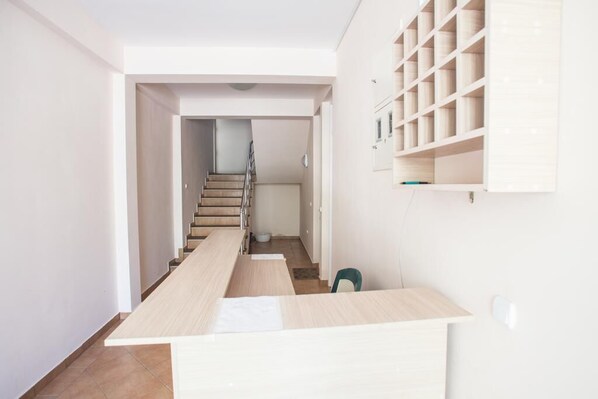 A narrow hallway with a wooden table and chairs, a staircase, and a white wall with shelves.