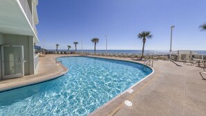 Une piscine aux eaux d’un bleu limpide, un bâtiment blanc et des palmiers.