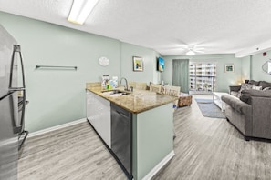 A modern kitchen with granite countertops, a dishwasher, and a dining area with a table and chairs.