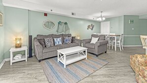 Un salon comprenant deux canapés, une table basse, un tapis à motifs et un coin repas avec une table et des chaises blanches.