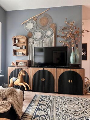 A modern living room with a television on a wooden cabinet, decorative wall art, and a horse figurine.