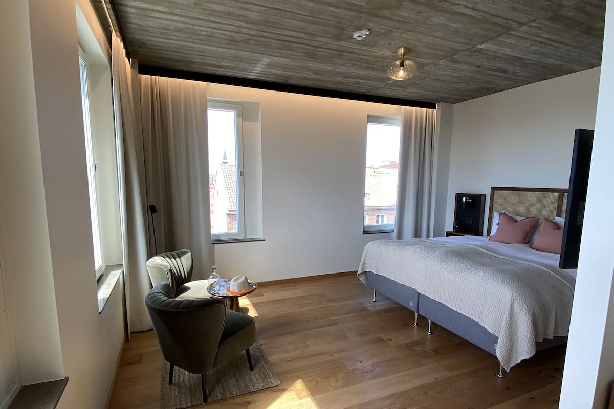 Een moderne hotelkamer met een groot bed, een bureau met stoel en uitzicht op de stad door de ramen.