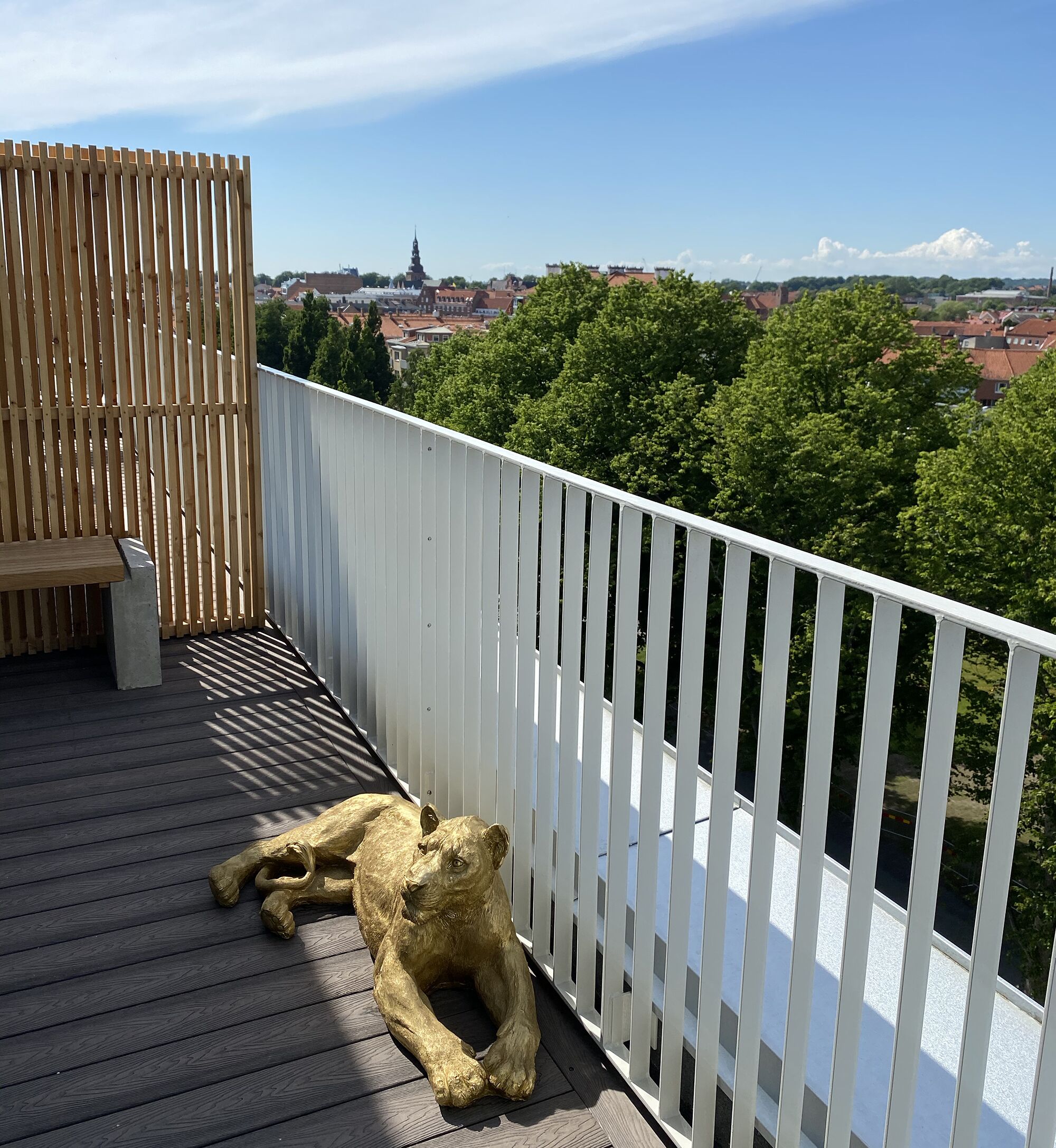 Una terraza de madera con baranda blanca que da a una vista panorámica de la ciudad, con una torre destacada.