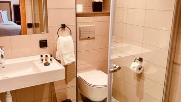 Ein modernes Badezimmer mit Duschkabine aus Glas, einem Waschbecken mit Pflegeprodukten und einer Toilette.