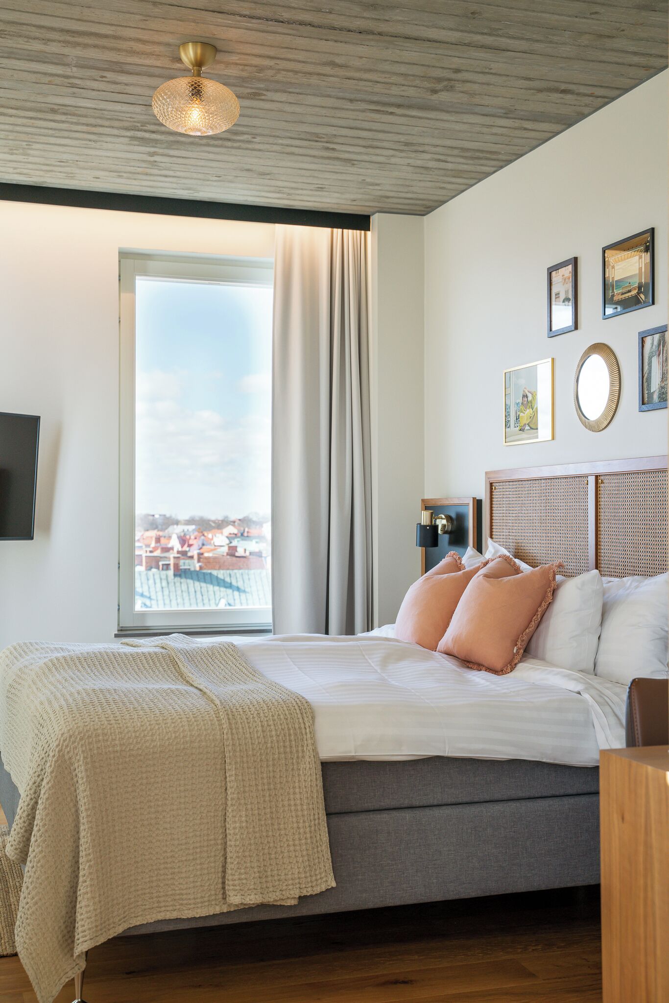 Un dormitorio con una cama grande, vistas de edificios a través de una ventana y una lámpara en el techo.